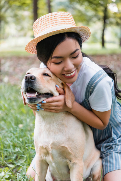 giovane e felice donna asiatica coccole giallo labrador nel parco - Foto, immagini