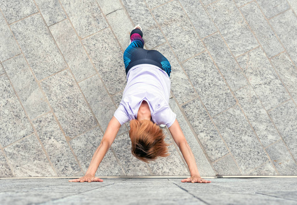 Urheilullinen nainen tekee venyttely harjoituksia jalkakäytävällä kaupungin näkymä ylhäältä hänen nojaten rakennuksen seinään kädet ojennettuna kunto käsite - Valokuva, kuva