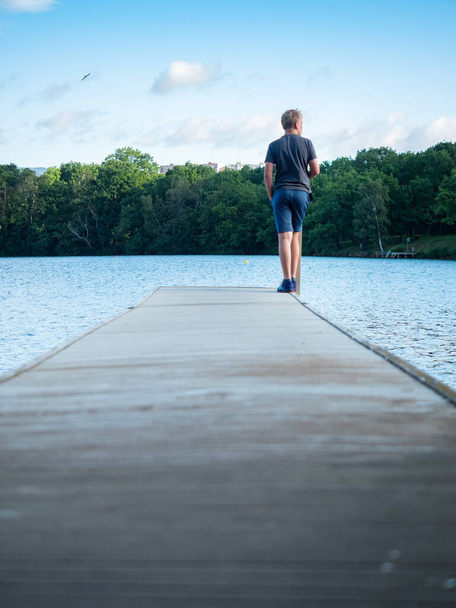 Мальчик останавливается на плавательном пирсе над квасным озером Каменково-Езеро в городе Хомутов.  - Фото, изображение