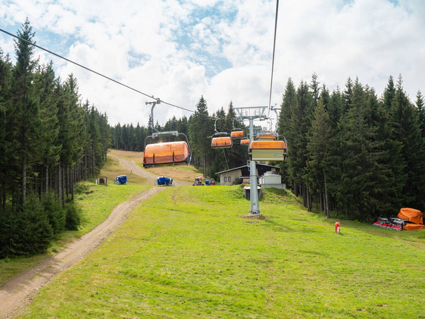 Chairlift with orange wind cover of seats shaking on the up way through forest. The downhill bike single track bellow lift. - Photo, Image