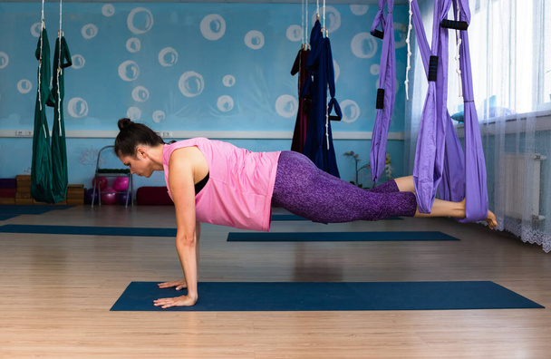 Spor kıyafetleriyle yoga yapan bir kadın stüdyoda hamakta egzersiz yapıyor. - Fotoğraf, Görsel