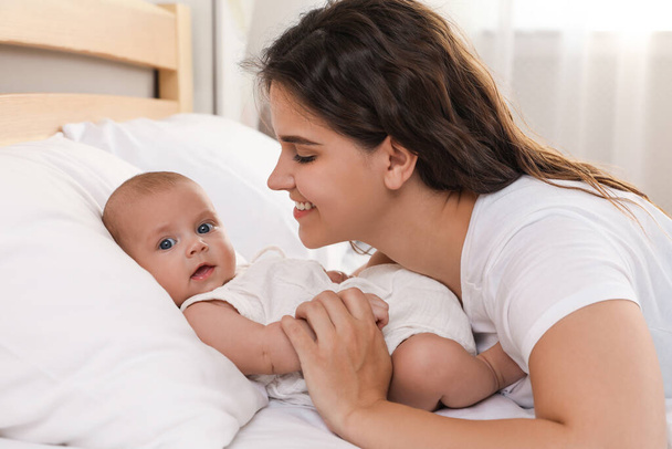 Happy young mother with her cute baby on bed at home - Foto, afbeelding