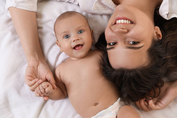 Happy young mother with her cute baby on bed, top view - Φωτογραφία, εικόνα
