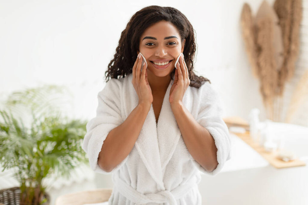 Femme noire posant avec des tampons de coton sur les joues dans la salle de bain - Photo, image