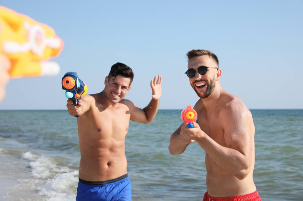 Friends with water guns having fun on beach - Foto, Bild