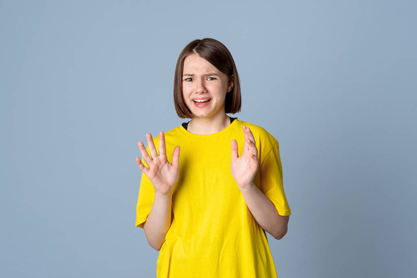Aghast teen girl in a panic standing over light grey background, wearing yellow t shirt. Emotions, people and lifestyle concept - Photo, Image