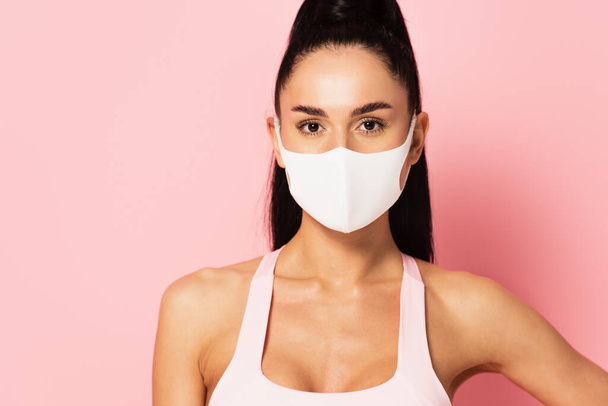 young sportswoman in medical mask looking at camera on pink  - Фото, зображення