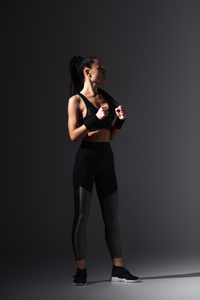 full length of strong young sportswoman standing with clenched fists on dark background  - Foto, Imagem