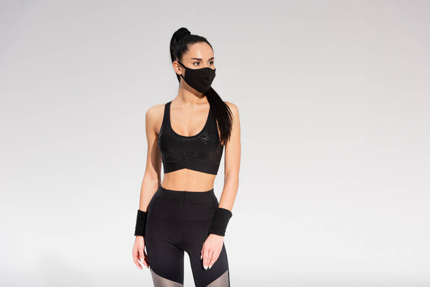 Spor giyimli genç bayan ve siyah koruyucu maske gri üzerinde duruyor. - Fotoğraf, Görsel