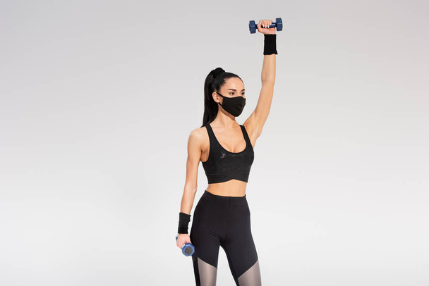 sportswoman in black protective mask working out with dumbbells on grey - Fotoğraf, Görsel