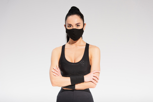 young sportswoman in sportswear and black protective mask standing with crossed arms on grey - 写真・画像