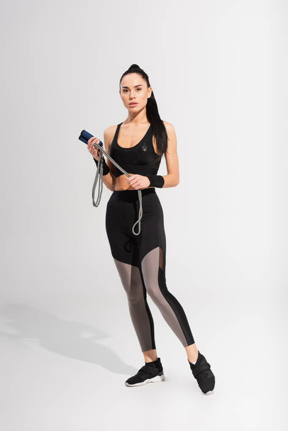 full length of young sportive woman holding skipping rope on grey - Photo, Image