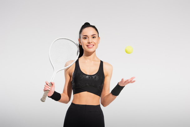 jonge sportvrouw met tennis racket en gooien bal op grijs - Foto, afbeelding