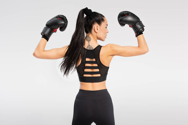 back view of tattooed sportswoman in boxing gloves isolated on grey - Photo, Image