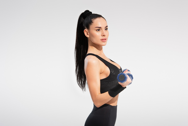 strong sportswoman in sportswear exercising with dumbbells isolated on grey - Photo, image