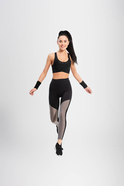 full length of smiling young woman in sportswear levitating on grey - Fotografie, Obrázek