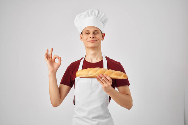 male baker in a white apron holding a loaf in hand cooking food - 写真・画像