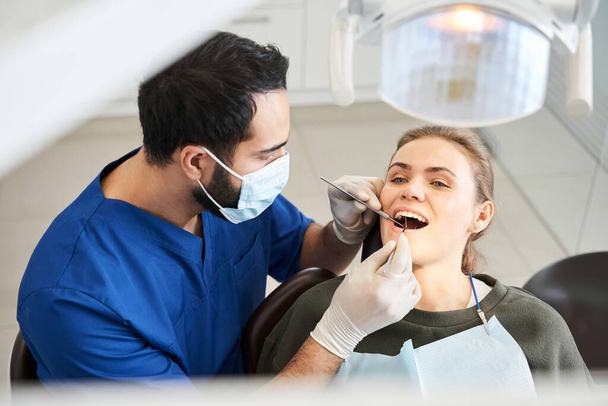 Blond-haired lady having her teeth examined by serious doctor - Foto, imagen