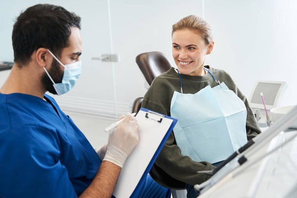 Serious male dentist talking with patient girl at dental clinic - Foto, immagini