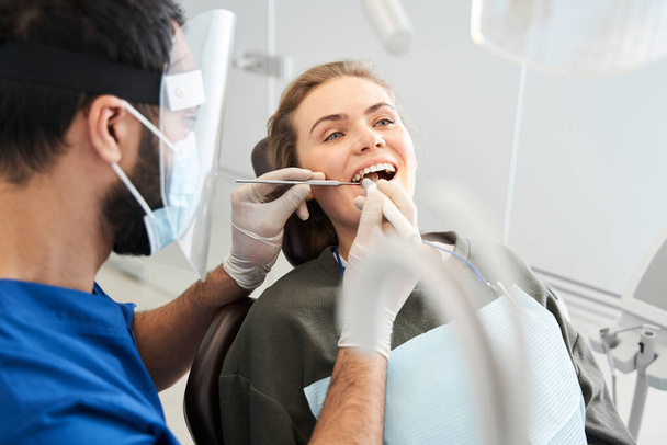 Serious male dentist in special uniform treating female client - Фото, зображення