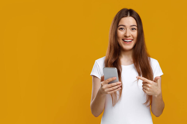 Emotional young woman pointing at new smartphone in her hand - Photo, Image