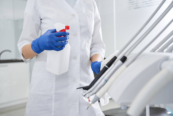 Dentist using antiseptic sanitizer, while cleaning stomatology equipment - Фото, изображение