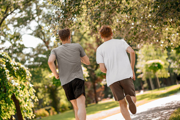 Guys running in park with backs to camera - Foto, Bild