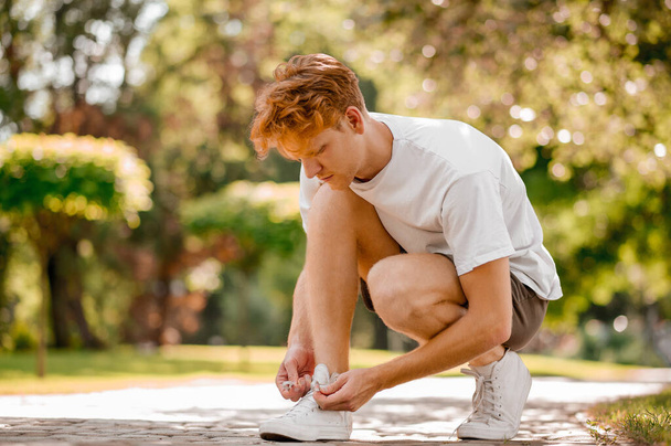 Ginger guy crouching tying shoelace on sneaker - Photo, Image