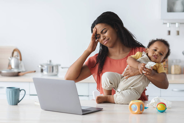Stresowana czarna matka z dzieckiem na rękach pracuje na laptopie w domu - Zdjęcie, obraz