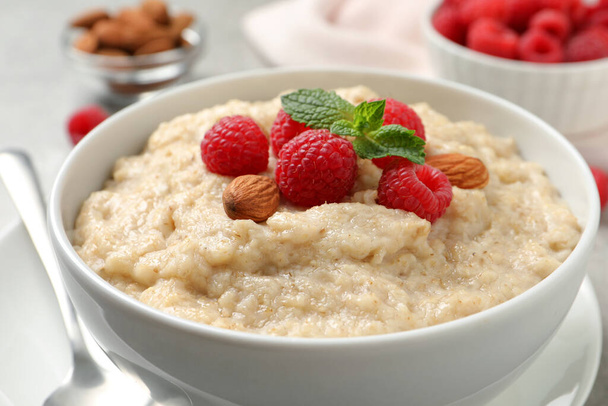 Tasty oatmeal porridge with raspberries and almond nuts in bowl on table, closeup - Photo, Image