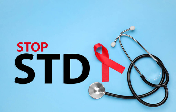 Red awareness ribbon, stethoscope and text Stop STD on light blue background, flat lay - Φωτογραφία, εικόνα