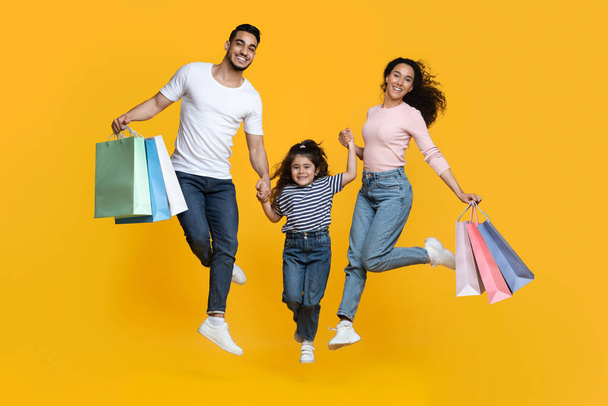 Gran concepto de compras. Alegre familia árabe de tres saltando con bolsas de comprador - Foto, imagen