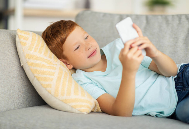 幸せな男の子ソファに横たわって、スマートフォンを使用して - 写真・画像