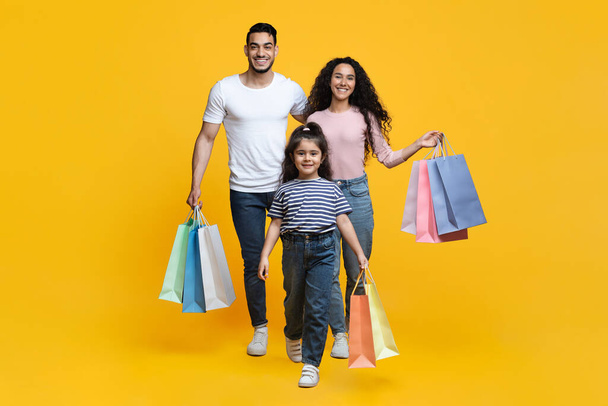 Giornata dello shopping. Allegro giovane famiglia mediorientale di tre a piedi con borse shopper - Foto, immagini