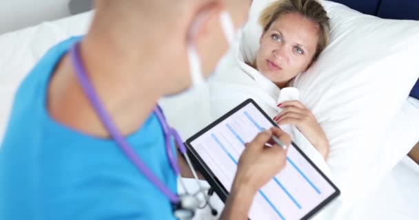 Γιατρός κάθεται δίπλα άρρωστος ασθενής ξαπλωμένος στο κρεβάτι και γράφει παράπονα σε ψηφιακή ταμπλέτα 4k ταινία - Πλάνα, βίντεο