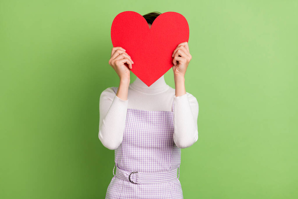 Photo of young girl close cover face big red paper heart card anonym incognito isolated over green color background - Fotó, kép