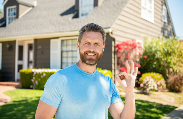 χαρούμενος ώριμος άντρας στέκεται έξω στο σπίτι δείχνει εντάξει, ευτυχία - Φωτογραφία, εικόνα