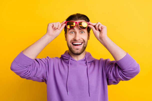 Photo of young excited man amazed shocked happy positive smile ahnds touch glasses isolated over yellow color background - Valokuva, kuva
