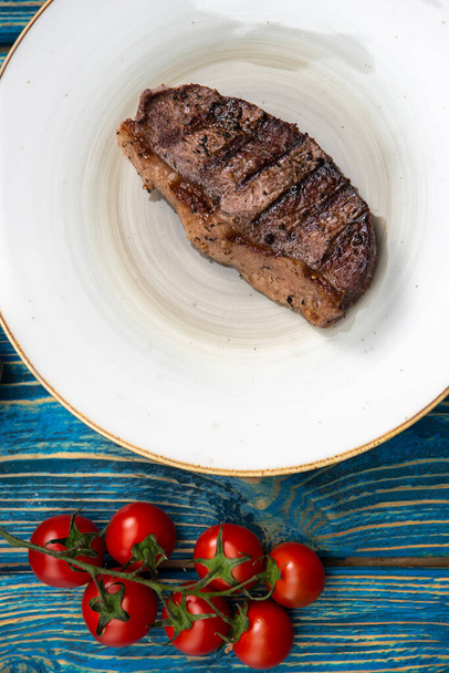 Roasted steak ,cherry tomatoes, salt and pepper on blue  wooden table. - Fotó, kép