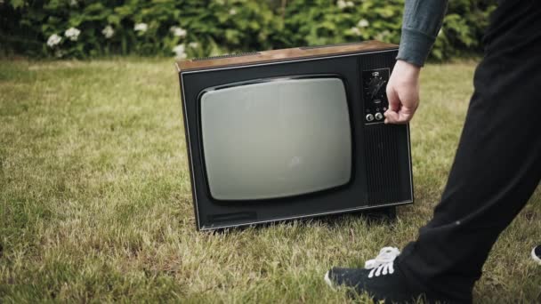 Man turns on old retro TV set standing on grass. Then person knocking the device - Footage, Video