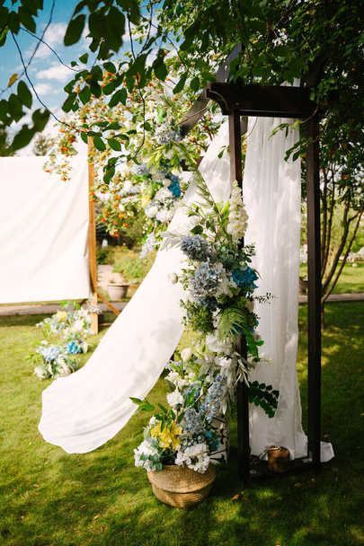 Beautiful wedding ceremony outdoors. Decorated chairs stand on the grass. Wedding arch made of cloth and white flowers on a green natural background. - Foto, Imagen