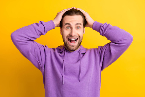 Photo of funky positive astonished guy hands head open mouth wear violet hoodie isolated yellow color background - Foto, Imagem