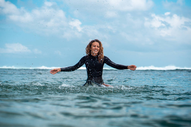 Portrait of surfer girl on white surf board in blue ocean pictured from the water in Bali - Фото, изображение