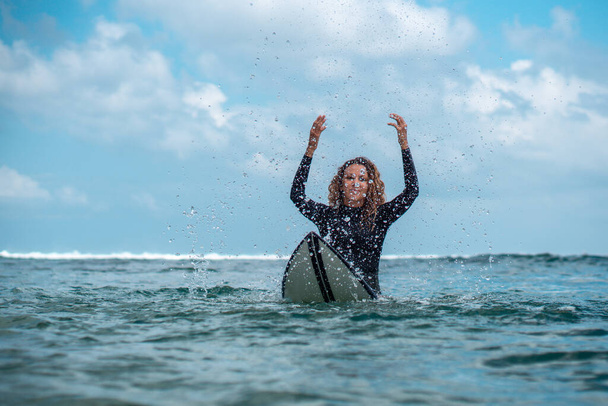 Portrait of surfer girl on white surf board in blue ocean pictured from the water in Bali - Fotografie, Obrázek