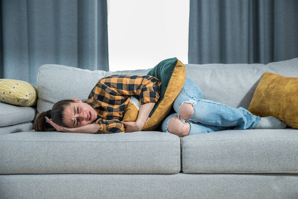 Young woman with menstruation is lying down on the couch and holding on to her stomach because she is in pain in the middle of menstrual cycle problems with painful facial expression, female issues  - Фото, изображение