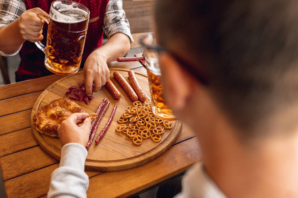 Close-up male hand with beer snacks and beer glasses during Octoberfest holiday meeting. Traditions, fun, joy, friendship, holidays. Oktoberfest, october, autumn concept - Фото, изображение