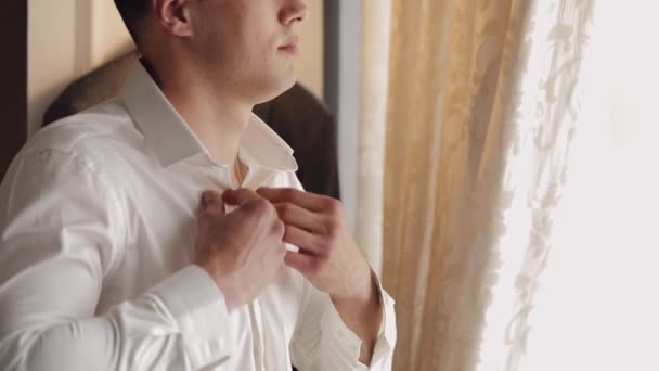 Κομψό άνθρωπος στο σακάκι στερεώνει τα κουμπιά, κουμπιά λευκό πουκάμισο ετοιμάζεται να βγει κοντά στο παράθυρο - Πλάνα, βίντεο