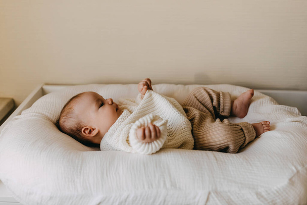 Baby draagt winterkleding, een warme gebreide trui en broek, liggend in een babynest. - Foto, afbeelding