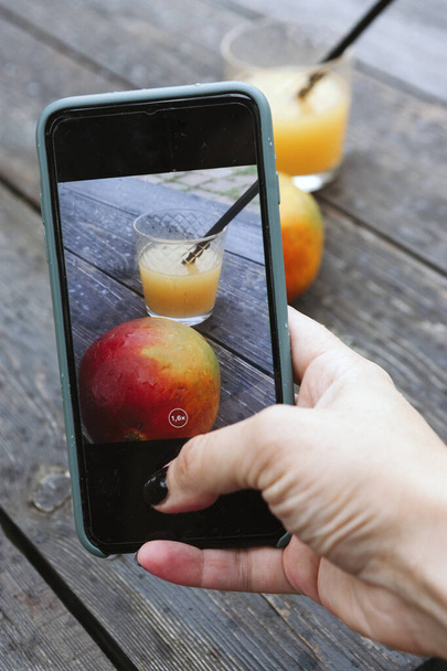 Γυναίκα λήψη φωτογραφιών του μάνγκο και χυμό στο κινητό τηλέφωνο - Φωτογραφία, εικόνα