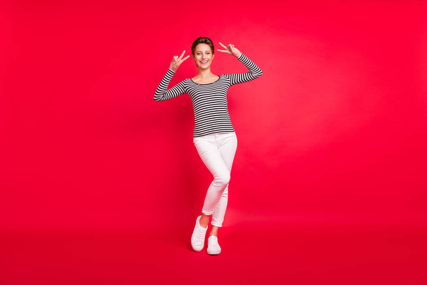 Photo of pretty adorable young woman dressed striped outfit smiling showing two v-signs isolated red color background - Φωτογραφία, εικόνα